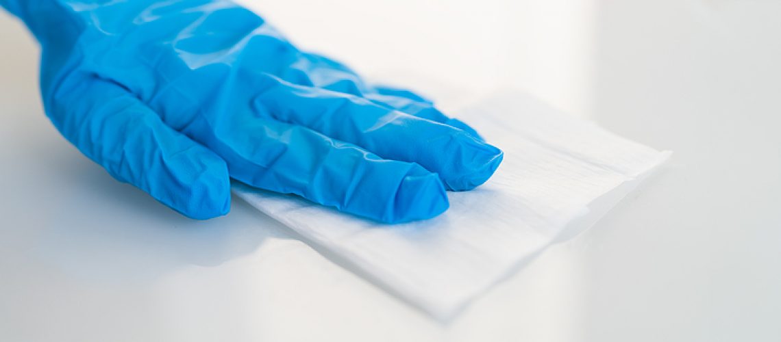 Surface cleaning against spreading of coronavirus person wearing gloves with antibacterial disinfecting wipe wiping glass table. banner panoramic background.
